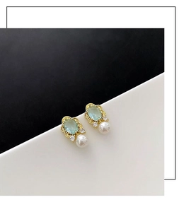 Detail view of light green oval gemstone stud earrings with gold trim and pearl drop