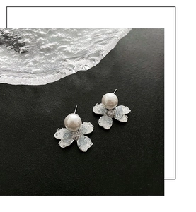 Close-up of pearl flower earrings with silver base and crystals on black matte background