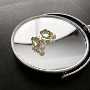 Elegant vintage light blue gemstone studs with pearl drop on a mirror reflection surface
