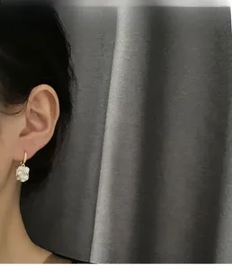 Close-up of elegant camellia drop earrings worn by model with gold hoop and white petal