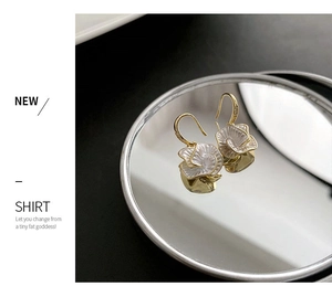 Close-up of golden camellia earrings with white petals reflecting on a mirror surface