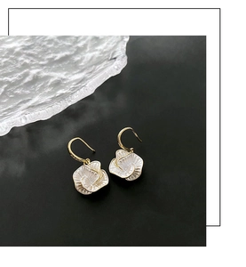 Detailed close-up of white flower-shaped earrings with elegant gold hooks on black background