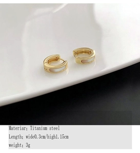 Détail de boucles d'oreilles en titane doré 18K avec incrustations d'émail blanc