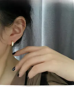 Gros plan d'une créole dorée minimaliste avec incrustation blanche sur l'oreille