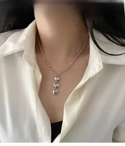 Détail du collier à trois pendentifs en cœur argentés avec chaîne à billes sur une chemise