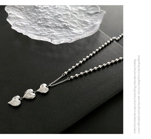 Vue détaillée du collier à billes argenté avec trois pendentifs en forme de cœur ciselé