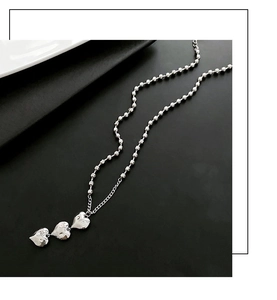 Détail du collier à perles argentées avec trois pendentifs en forme de cœur texturé