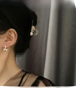 Detail einer weißen Schleifenohrring aus Emaille mit kleinen Diamanten am Modell vor grau