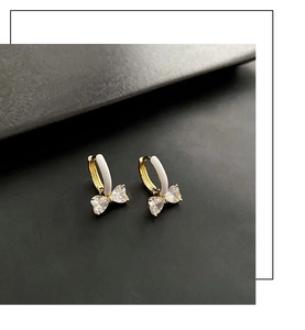Detail von goldenen Creolen mit weißem Emaille-Finish und funkelnden Zirkon-Schleifen
