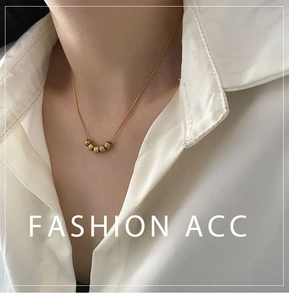 Detail of five gold frosted beads on a delicate snake chain necklace worn with a white shirt