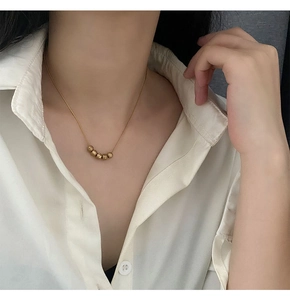 Detail shot of a minimalist gold necklace with five textured gold beads on model