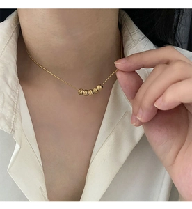 Close-up of a elegant gold necklace with five matte textured beads on a female model
