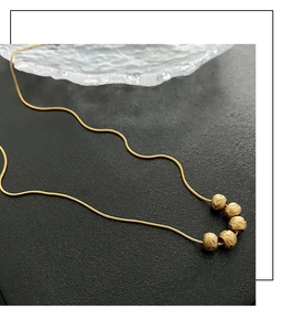 Detailed view of vintage gold snake chain necklace with five textured beads on black background