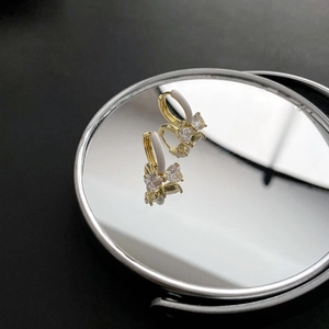 Elegante goldene Schleifenohrringe mit Zirkonia und weißem Emaille auf schwarzem Spiegel