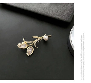 Détail macro d'une broche tulipe dorée avec zircons en goutte et une perle blanche