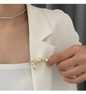 Détail d'une broche tulipe dorée élégante avec perles et strass sur un blazer blanc