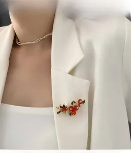 Modèle portant une broche vintage avec perles rouges et feuilles vertes sur blazer blanc