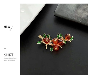 Détail de la broche vintage avec branches dorées et perles rouges sur fond noir mat