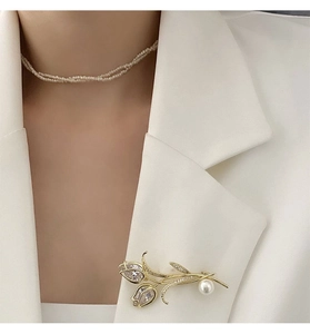 Détail d'une broche tulipe de luxe avec placage or, zircons et perle blanche sur un blazer chic