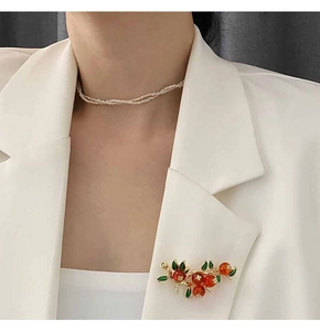 Détail d'une broche kaki avec perles oranges et collier de perles sur un costume blanc