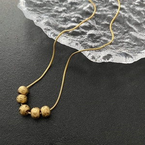 Vintage gold snake chain necklace with five matte textured beads on a glass plate