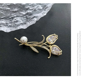 Détail macro d'une broche tulipe en métal doré avec perle blanche et cristaux brillants