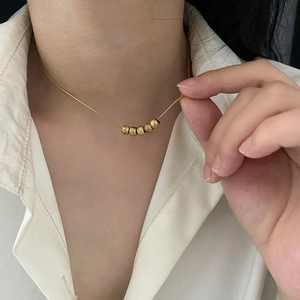 Vintage gold necklace featuring five matte texture beads on female model in white shirt
