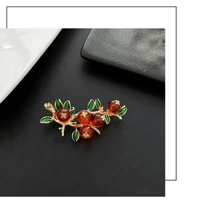 Vue détaillée d'une broche branche dorée vintage avec baies rouges et feuilles d'émail