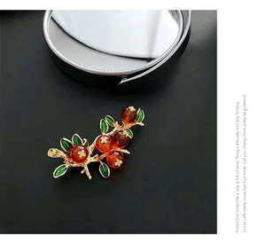 Détail de la broche vintage avec fruits en résine rouge et feuilles en émail vert