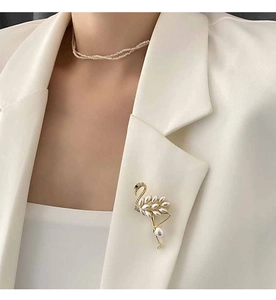 Detail of elegant swan brooch with pearls and matching necklace on a white blazer