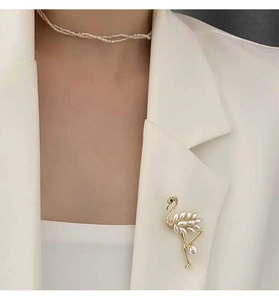 Detailed close-up of flamingo brooch with white pearls on a white blazer collar