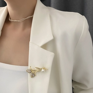 Élégante broche tulipe dorée avec zircons et perle sur le revers d'un blazer blanc