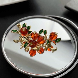 Broche persimmon exquise avec branches dorées et perles orange sur un miroir élégant