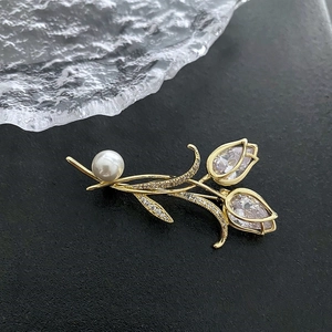 Broche tulipe dorée élégante avec des strass en poire et une perle sur un fond gris foncé