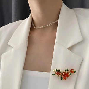 Broche kaki élégante avec fruits orange et feuilles vertes sur une veste de costume