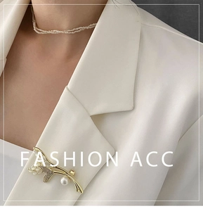 Détail d'une broche tulipe dorée avec perle blanche et zircons sur revers de veste