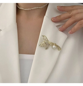 Détail d'une broche queue de poisson avec opale, zircons et perle pendante sur un blazer