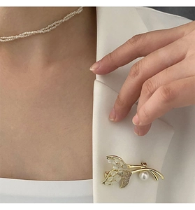 Détail de l'élégante broche fleur en or avec nacre et perle sur un blazer blanc chic