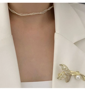 Détail d'une broche opale queue de poisson et collier de perles sur blazer blanc