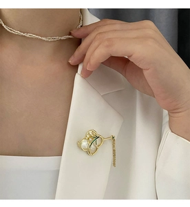 Detail einer Orchideenbrosche mit Perlmutt und Quasten an einem weißen Blazer