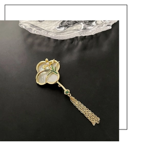 Detail einer Orchideen-Brosche mit weißen Muschel-Blüten und langen Goldquasten auf Schwarz