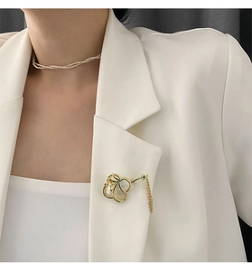 Detaillierte Orchideen-Brosche mit Perlmutt und goldener Quaste auf weißem Blazer