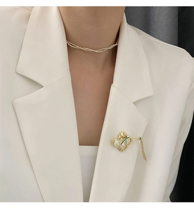 Detail einer Gold-Orchideen-Brosche mit Muschel-Inlay und Kettentroddel auf einem Blazer
