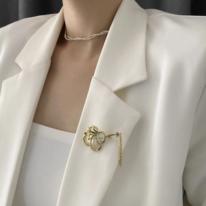 Elegante goldene Orchideen-Brosche mit Perlmutt-Blüten und Quaste auf weißem Blazer