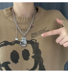 Detail der silbernen Fu-Halskette mit Herzanhängern auf einem khakifarbenen Pullover