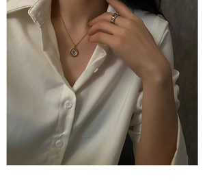 Detail view of gold coin pendant necklace and silver chain ring on white satin shirt