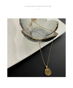 Detail shot of golden necklace with embossed elephant coin pendant on glass bowl