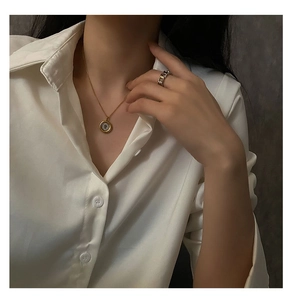 Close-up of golden coin necklace and silver chain ring styled with white satin shirt