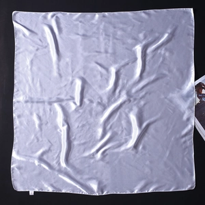 Détail d'un foulard carré en satin blanc montrant une texture brillante et des ourlets