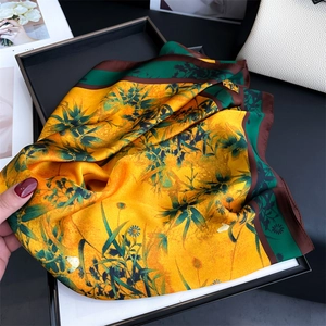Detail of silk-like square scarf featuring yellow bamboo leaf prints in a black gift box